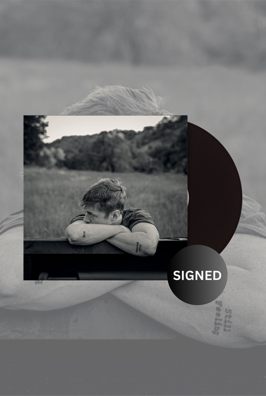 A black and white image of a vinyl LP with a 'Signed' label, showing a person lying down next to a record.
